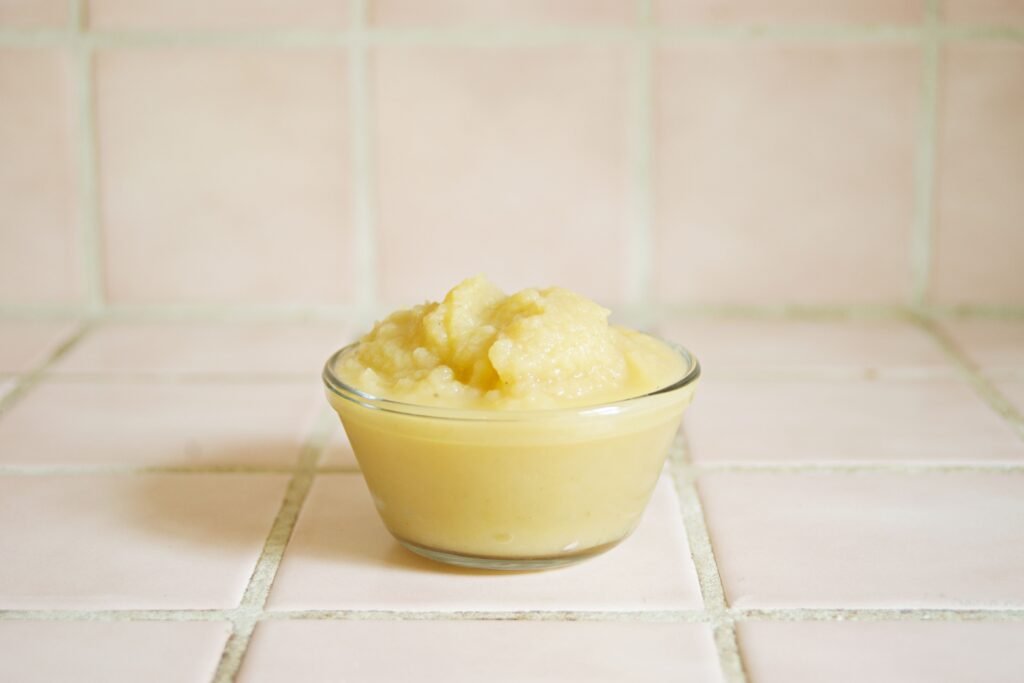 Close-up of homemade applesauce in a clear glass bowl on a tiled surface.